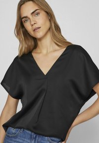 Blusa nera in satin con scollatura a V, maniche corte e vestibilità ampia. Presenta un delicato dettaglio di piegatura sul davanti e una texture morbida.