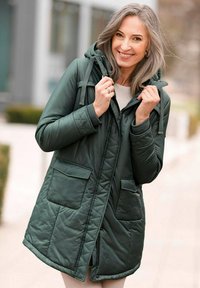 Dunkelgrüne gepolsterte Jacke mit Kapuze, ausgestattet mit einem Reißverschluss, zwei Vorderstaschen und strukturiertem Stoff mit einem gesteppeten Design.