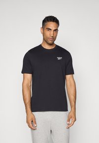 T-shirt en coton noir à manches courtes et col rond, arborant un petit logo Reebok blanc sur la poitrine gauche.