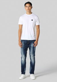 White cotton t-shirt with a small black logo, paired with blue distressed denim jeans and white sneakers. Simple, casual style.