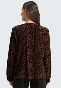 Blouse marron à manches longues avec un imprimé léopard noir, tissu doux et encolure dos froncée avec détails boutonnés.