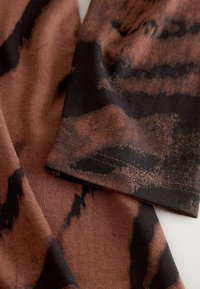 Tissu brun et noir à motif avec des sections qui se chevauchent et une texture douce. Les coutures sont visibles le long des bords.