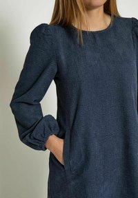 Navyblaues, strukturiertes Kleid mit langen Puffärmeln, Rundhalsausschnitt und seitlichen Taschen. Der Stoff hat ein geripptes Muster.