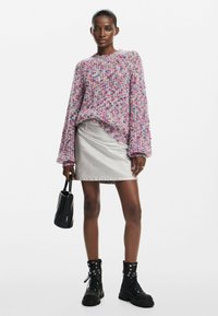 Több színben készült kötött pulóver, laza fazonnal és texturált mintával, fémes ezüst farmer szoknyával és fekete fűzős katonai csizmával párosítva.