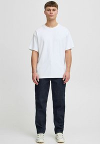 White crew-neck T-shirt, relaxed fit, paired with dark blue straight-leg jeans and white sneakers featuring a subtle pattern on the side.