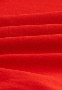 Roter Stoff mit einer glatten Textur, in Falten angeordnet. Das Material wirkt leicht und besteht aus einer einheitlichen, soliden Farbe ohne Muster.