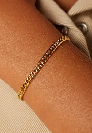 Gouden kettingarmband op een huidkleurige pols, met in elkaar grijpende schakels met een gladde, glanzende afwerking en een subtiele textuur.