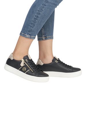 Baskets en cuir noir avec des accents en daim beige, semelle blanche, détail de fermeture éclair dorée et design à lacets, posées sur un jean en denim bleu.