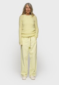 Maglione fuzzy giallo chiaro abbinato a pantaloni larghi giallo pastello. Tessuto morbido con un design rilassato e vita con cordoncino. Scarpe bianche.