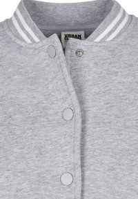 Gros plan sur un sweat-shirt gris clair avec un col côtelé à rayures blanches et des boutons-pression le long de l'ouverture frontale.