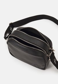 Borsa a tracolla nera in pelle con tre scomparti con zip, tracolla regolabile con logo, superficie strutturata e forma rettangolare.