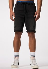 Shorts de mezclilla negros con un patrón desgastado, cinturilla ajustable, dobladillos enrollados y bolsillos, combinados con zapatillas blancas de caña alta.