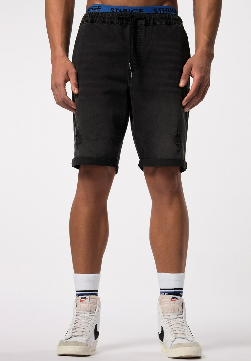 Shorts de mezclilla negros con un patrón desgastado, cinturilla ajustable, dobladillos enrollados y bolsillos, combinados con zapatillas blancas de caña alta.