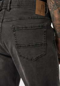 Sorte denim jeans med en struktureret overflade, baglommer med vandret syning og et brunt lædermærke i taljen.