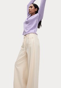 Pantaloni crema dal fitting morbido con vita regolabile e tasche laterali, abbinati a un maglione leggero viola chiaro con dettagli laterali.