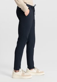 Marineblauwe stretchbroek met een trekkoord in de taille, zijzakken en een subtiele textuur. Draag het met lichtgekleurde sneakers met een beige accent.
