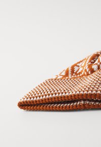 Strickmütze in Orange und Weiß mit geometrischen Mustern, die eine strukturierte Oberfläche und einen umgeschlagenen Rand für einen bequemen Sitz aufweist.