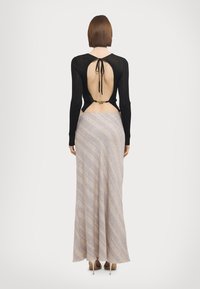 Black long-sleeve top with open back and tie detail, paired with a beige maxi skirt featuring diagonal stripes and frayed hem.