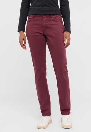 Burgunderfarbene Baumwollhose mit geradem Schnitt, ausgestattet mit fünf Taschen, einem Bund mit Gürtelschlaufen und minimalen Nähten. Kombiniert mit weißen Sneakers.