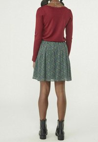 Červený top s dlouhým rukávem a kulatým výstřihem, doplněný vzdušnou zelenou sukní s květinovým vzorem a černými kotníkovými botami.