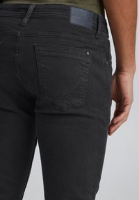 Černé džíny z denimu s úzkým střihem, opatřené zadními kapsami, logem na pásku a jemnými švy. Hladká textura.