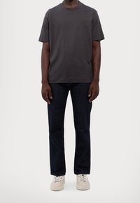 Gray cotton t-shirt with short sleeves, round neckline, and minimal branding. Paired with dark denim jeans and light-colored sneakers.