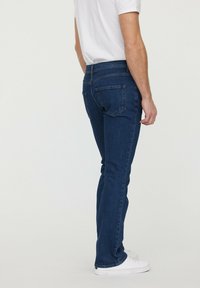 Jeans en denim bleu foncé avec une coupe droite, dotés de poches arrière et d'une taille standard. Le tissu a une finition lisse et texturée.
