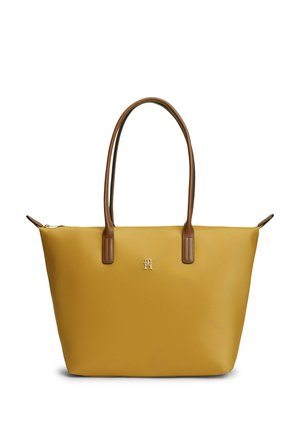 Gul tote-taske med brune læderhåndtag og et lille metallisk logo centreret nær toppen, vist mod en hvid baggrund.