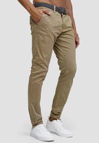 Pantalones slim-fit beige de mezcla de algodón, con cierre de botón y cremallera, bolsillos laterales y un cinturón negro con estampado.