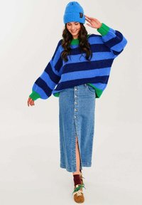 Pruhovaný modro-zelený pletený svetr s širokými rukávy, v kombinaci s modrou džínovou sukní s předním rozparkem a knoflíky. Hnědé boty se zelenými akcenty.