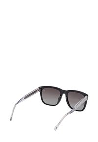 Svarta rektangulära solglasögon med gradientmörka linser och genomskinliga klara skalmar, visade vinklat mot en vit bakgrund.