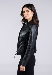 Giubbotto da moto in pelle nera con chiusura a zip, dettagli decorativi sulle spalle e design minimalista con una texture liscia.