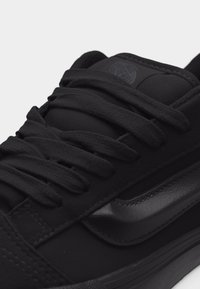 Μαύρο αθλητικό παπούτσι Vans με χοντρές κορδόνια και υφασμένη δερμάτινη λωρίδα στο πλάι, κοντινή λήψη στην πάνω και στη γλώσσα όπου φαίνεται το λογότυπο.