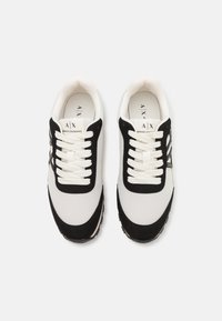 Black and white athletic sneakers with mesh upper, suede accents, and white laces. Features a logo on the tongue and a textured sole.