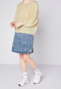 Helles gelbes, übergroßes Sweatshirt aus weichem, flauschigem Material, kombiniert mit einem mittel-langen Jeansrock in Blau, der ein dreieckiges Logo-Patch aufweist.