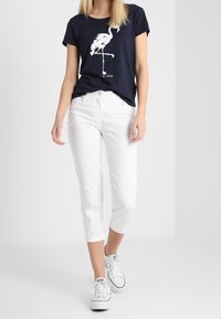 Granatowy t-shirt z białą grafiką flaminga, w zestawieniu z białymi spodniami typu crop i białymi sneakersami. Bawełnowy materiał, luźny krój, krótki rękaw.