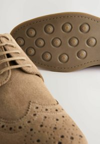 Vaaleanruskeat sueded kengät, joissa on brogue-yksityiskohtia, pyöreä kärki ja tekstiilivärityksellä varustettu kumipohja, jossa on pyöreitä tartuntavarsi.