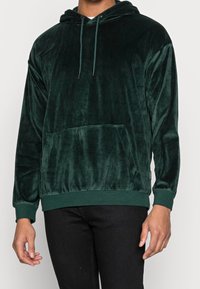 Grön velourhoodie med framficka, justerbar dragsko i huvan och ribbade mudd och nederkant för en avslappnad passform.