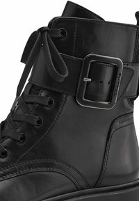 Černá kožená kotníková bota s kulatou špičkou, předními šněrováním, přezkou na kotníku a hladkým povrchem s jemnými švy.