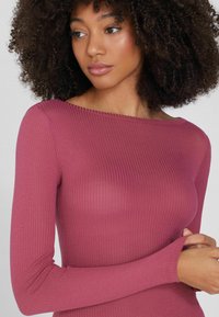 Geripptes Langarmoberteil aus weichem Mauve-Stoff, mit einem Bootsausschnitt und figurbetontem Schnitt, das eine dezente Textur und ein anliegendes Design aufweist.