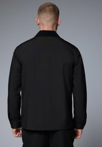 Chaqueta negra con collar, mangas largas y detalles de botones. Hecha de una tela suave, cuenta con un diseño limpio en la parte posterior sin adornos.