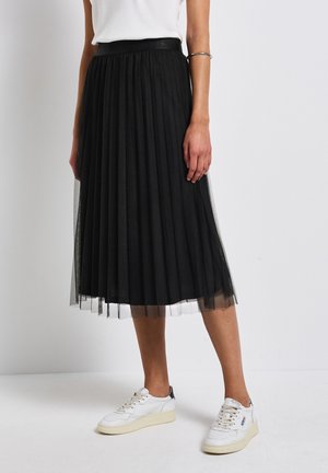 Gonna midi nera plissettata con sovrapposizione di tulle trasparente, vita elastica e texture liscia, abbinata a sneakers bianche.