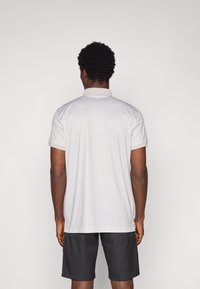 Polo gris clair avec une texture à motif subtil, manches courtes et un col contrasté, associé à un short noir.