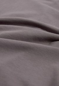 Tissu gris avec une texture lisse, présentant des plis et des rides subtils, indiquant un matériau léger et extensible.