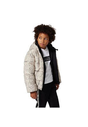 Veste rembourrée de couleur crème avec une inscription graphique noire, dotée d'une capuche et d'une fermeture éclair, superposée à une chemise blanche avec du texte noir, associée à un pantalon noir.