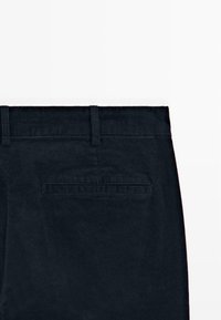 Vue arrière d'un pantalon en velours côtelé noir montrant la taille avec passants de ceinture et une poche passepoilée sur fond blanc.
