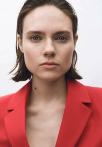 Punainen räätälöity bleiseri, sileä kangas, sakarat, tiukka istuvuus. Mallilla on lyhyet hiukset ja vaalea iho, neutraali tausta.