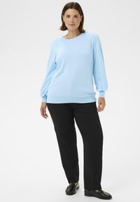 Hellblauer Pullover mit langen Ärmeln, rundem Ausschnitt, geripptem Saum und Bündchen, kombiniert mit schwarzen Hosen mit geradem Bein und schwarzen Loafers.