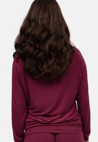 Bordeaux lange mouwen top met een ontspannen pasvorm en zachte textuur, voorzien van een ronde hals en een achterlengte die elegant valt.