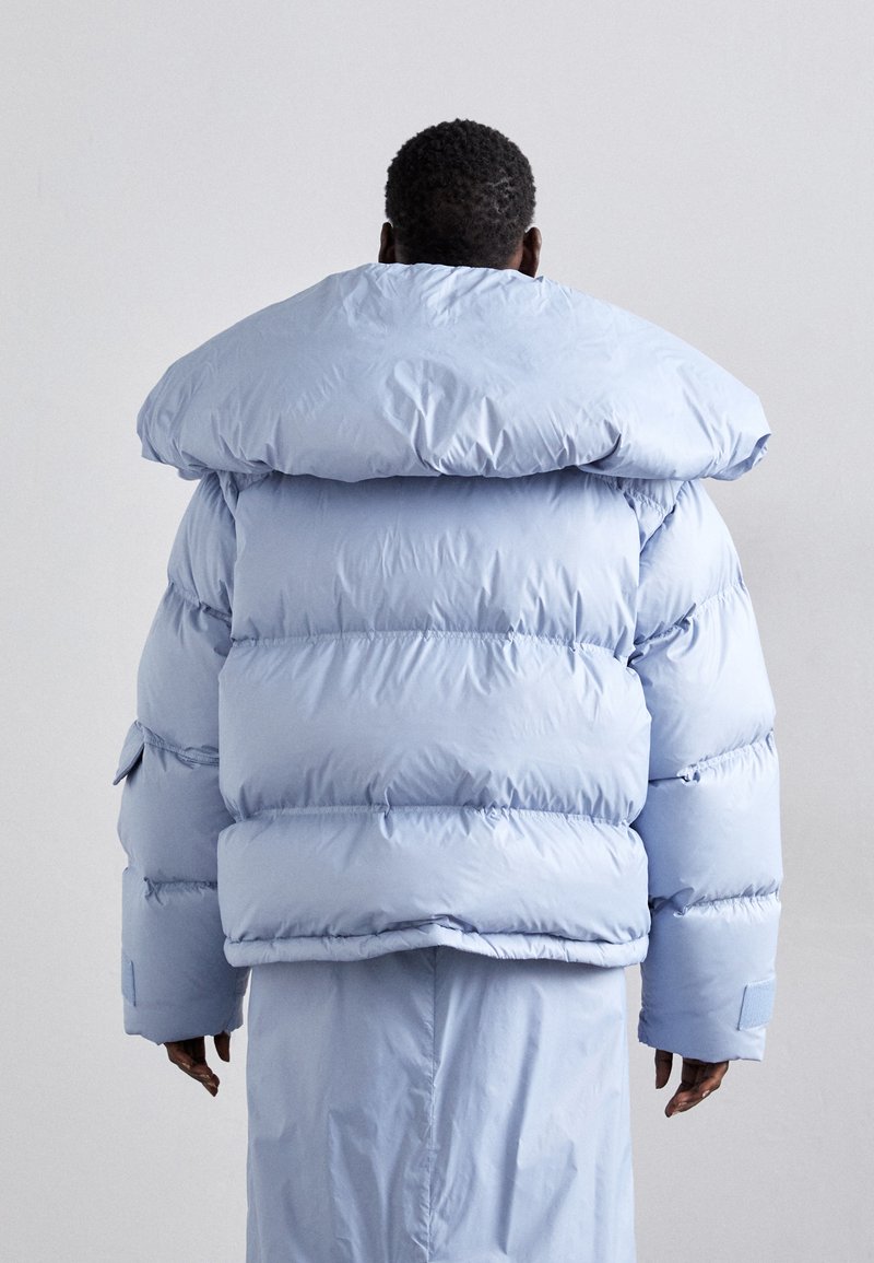 Doudoune bleu clair avec capuche oversize, motif matelassé et poignets élastiques. Tissu doux et brillant avec une coupe décontractée.